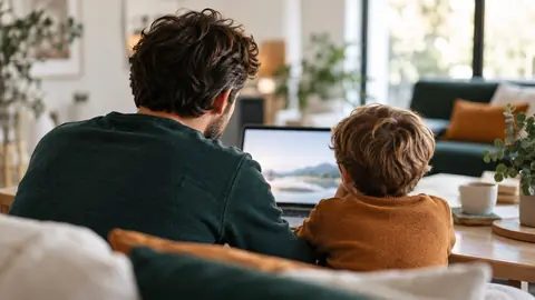 Adulte et enfant vus de dos devant un écran d'ordinateur portable dans un salon